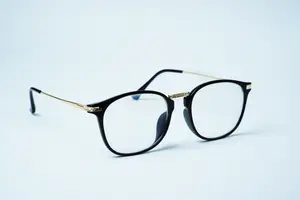 A pair of black glasses with golden frames on a white surface