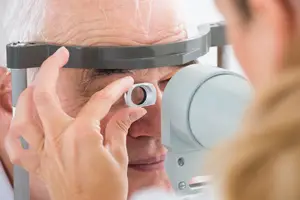 An older hartland mi patient is having his eyes examined by an eye doctor using an ophthalmoscope.
