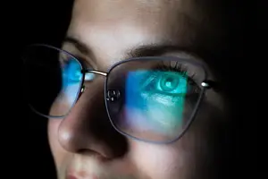 Close-up of a woman's eye reflected in her glasses with a green glow