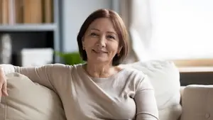 A woman with short hair and a smile on her face is sitting on a couch in her living room.