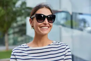 A woman smiling and wearing sunglasses and a striped shirt.