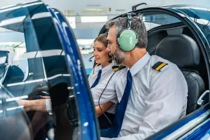 A man and a woman are sitting in the cockpit of an airplane wearing headphones and uniforms