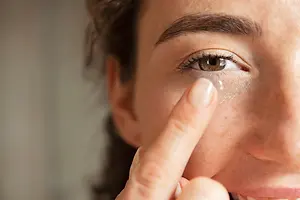 A woman wearing a contact lens on her eye with her finger touching the lens