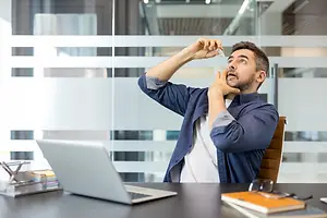 Man applying eye drops while seated at a desk