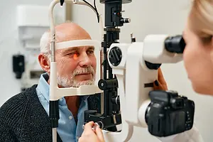 Optometrist examining an older man with a slit lamp eye examination device