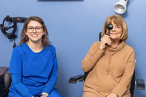 Two women in a medical office, one holding an eye exam tool, smiling at the camera.