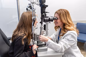 An optometrist checks a young patient's eyes using an ophthalmoscope