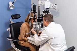 A female patient undergoing an eye exam by a male optometrist using an ophthalmoscope