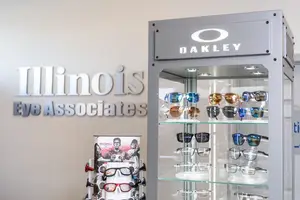 An Oakley sunglasses display with the brand name and Illinois Eye Associates logo on the wall in a retail setting