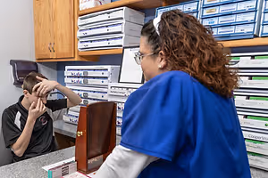 A woman in a blue lab coat is examining a boy's eyes in a medical office.