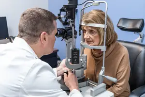 An optometrist is examining a patient's eyes with an ophthalmoscope in a clinical setting.
