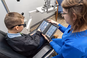 A boy is having an eye exam with a woman who is assisting him.