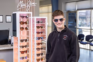 A smiling man stands behind a Maui Jim sunglasses display in a store.