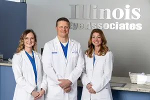 Three eye doctors wearing white coats standing in front of an Illinois Eye Associates sign