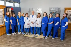 A group of medical professionals in blue uniforms stand in front of a wall with the words Illinois Eye Associates, smiling for a photograph.