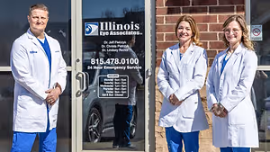 Three people are standing in front of the building of Illinois Eye Associates with their hands in their pockets