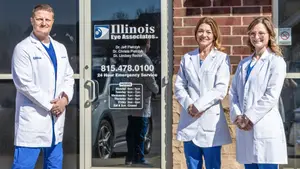 Three people are standing in front of the building of Illinois Eye Associates with their hands in their pockets