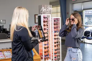 Two women standing in front of a sunglasses display in a store with the word Maui Jim on it
