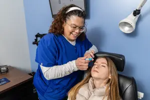 A woman is getting a procedure done by another woman who is wearing a blue uniform and glasses in a blue room
