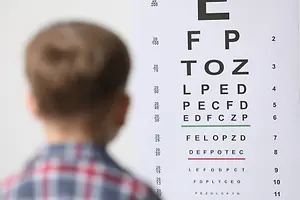 A young boy with a red and blue checkered shirt is looking at an eye chart on a wall with different letters and numbers