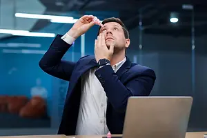 Businessman applying eye drops while looking upward
