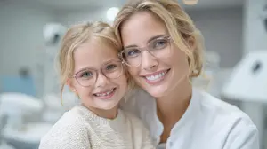 A woman wearing glasses and a white shirt is hugging a young girl wearing glasses and a white sweater