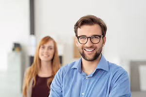 A smiling man with glasses and a woman with long hair in a room with white walls