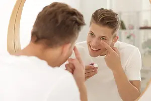 Man looking in mirror while applying eye cream.