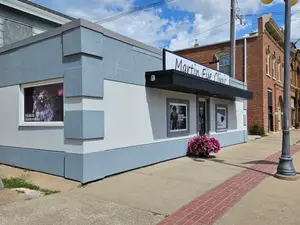 A building with a name board that reads Martin Eye Clinic in front of a brick building with a sidewalk and a flower vase.