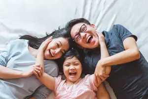 A joyful family of three lying on a bed, smiling and laughing together.