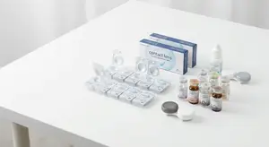 A collection of contact lens products on a white table, including lens cases, solution bottles, and a box of contact lenses.