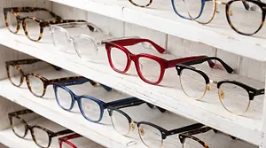 Close-up of a row of eyeglasses, including red frames, displayed on a white wooden shelf.