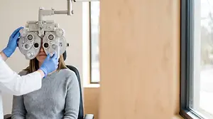 A woman in a doctor's office getting her eyes checked by a doctor wearing blue gloves.
