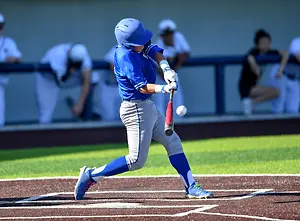 A baseball player in a blue and gray uniform swings his bat at a ball thrown by the pitcher