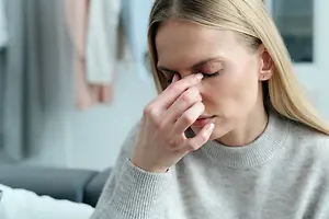 A woman sitting on a couch and covering her nose with her hand, probably in a living room
