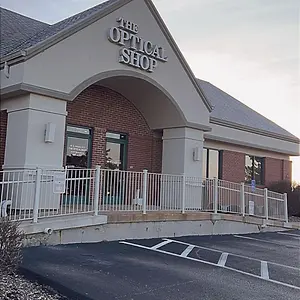The Optical Shop located in Grand Junction, CO, has a white railing, brick walls, and a glass door, with a clear sky as the backdrop.