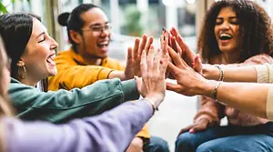 A group of four young adults smiling and giving each other high fives in an indoor setting