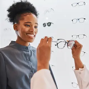 A woman is trying on glasses in a store with a doctor, smiling as she looks through the glasses.