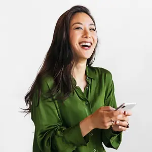 A smiling woman wearing a green blouse and holding a phone in her right hand and her left hand is holding a ring.