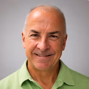 An older man with a bald head and wearing a green polo shirt is smiling and posing for a picture