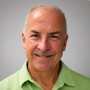 An older man with a bald head and wearing a green polo shirt is smiling and posing for a picture