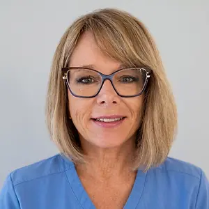 Photo of a woman with short blonde hair, wearing glasses and a blue shirt, smiling.