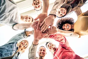 Group of friends with hands together in a circle, smiling at the camera