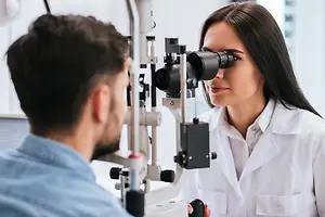 A woman in a lab coat examining a man's eyes with an ophthalmoscope