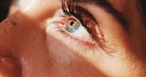 Close-up of a woman's eye with brown iris, eyelashes, and freckles on her face.