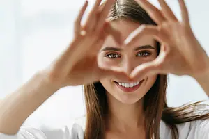 A woman making a heart shape with her hands and smiling for the camera.