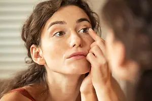 Close up of a woman looking in the mirror adjusting her eyelashes.