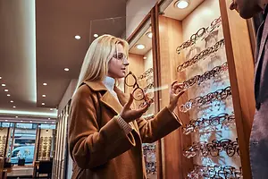 A woman is looking at eyeglasses with a man in front of a wooden display case