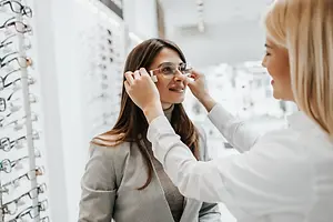 A woman is adjusting glasses while another woman adjusts her glasses in a store
