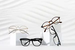 A selection of glasses placed on a white surface, including a pair with brown frames and a tortoise pattern, a pair with black frames, and another with a black frame and brown lenses